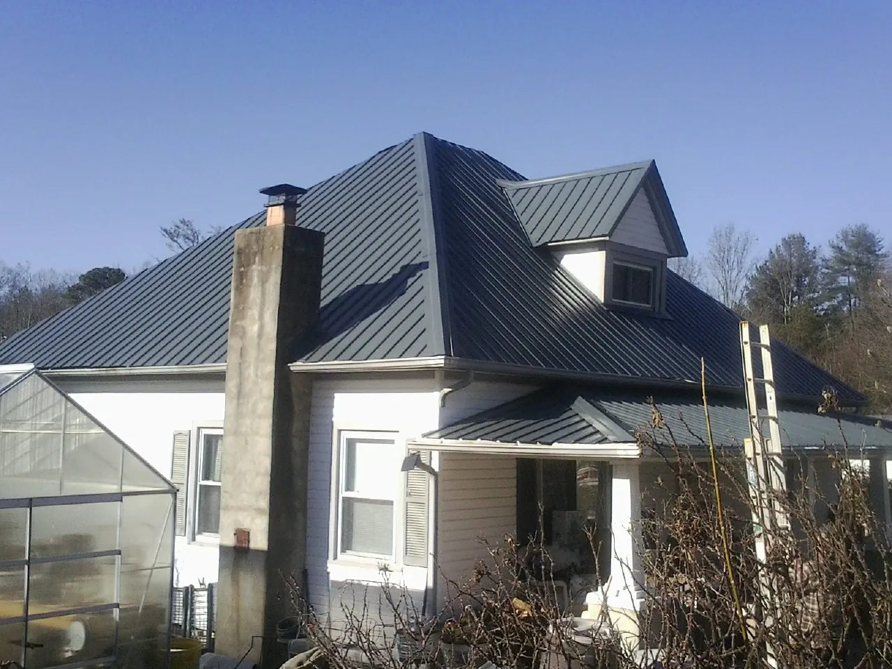 Dark blue standing seam metal roof on a white farmhouse with dormer — Slate & Tile Roof Repair by Roofing Brothers in Kasson