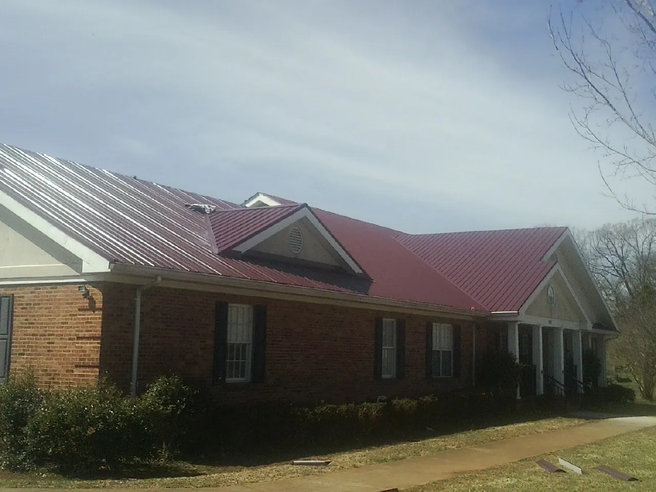 Red metal roof with gabled entries on a long brick building, from a Hail Damage Roof Repair job in Kasson