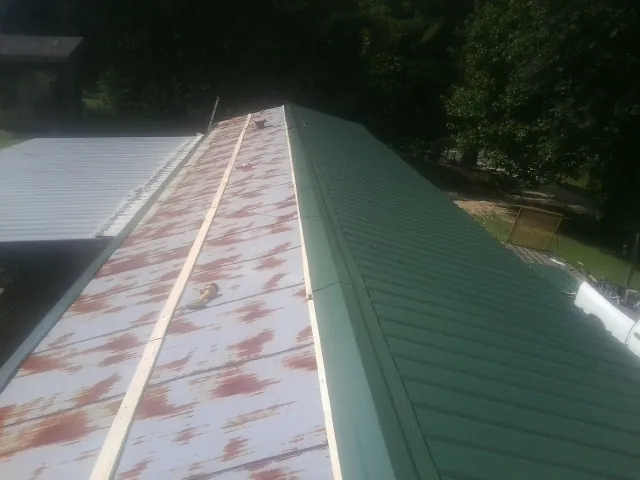 Old rusted panels beside newly installed green metal roofing — Wind Damage Roof Repair by Roofing Brothers in Kasson