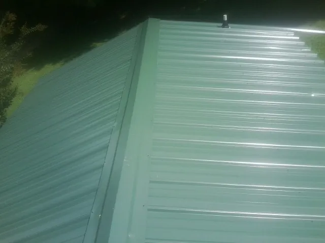New green metal panels meeting at the ridge of a roof — Flat Roof Repair work by our crew in Kasson