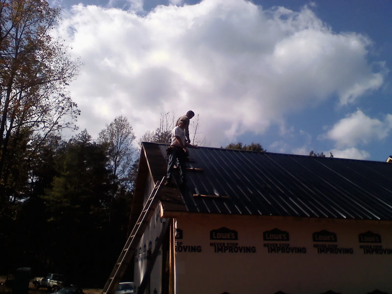 Roofer fastening dark metal panels high against a cloudy sky, from a Roof Inspection job in Kasson