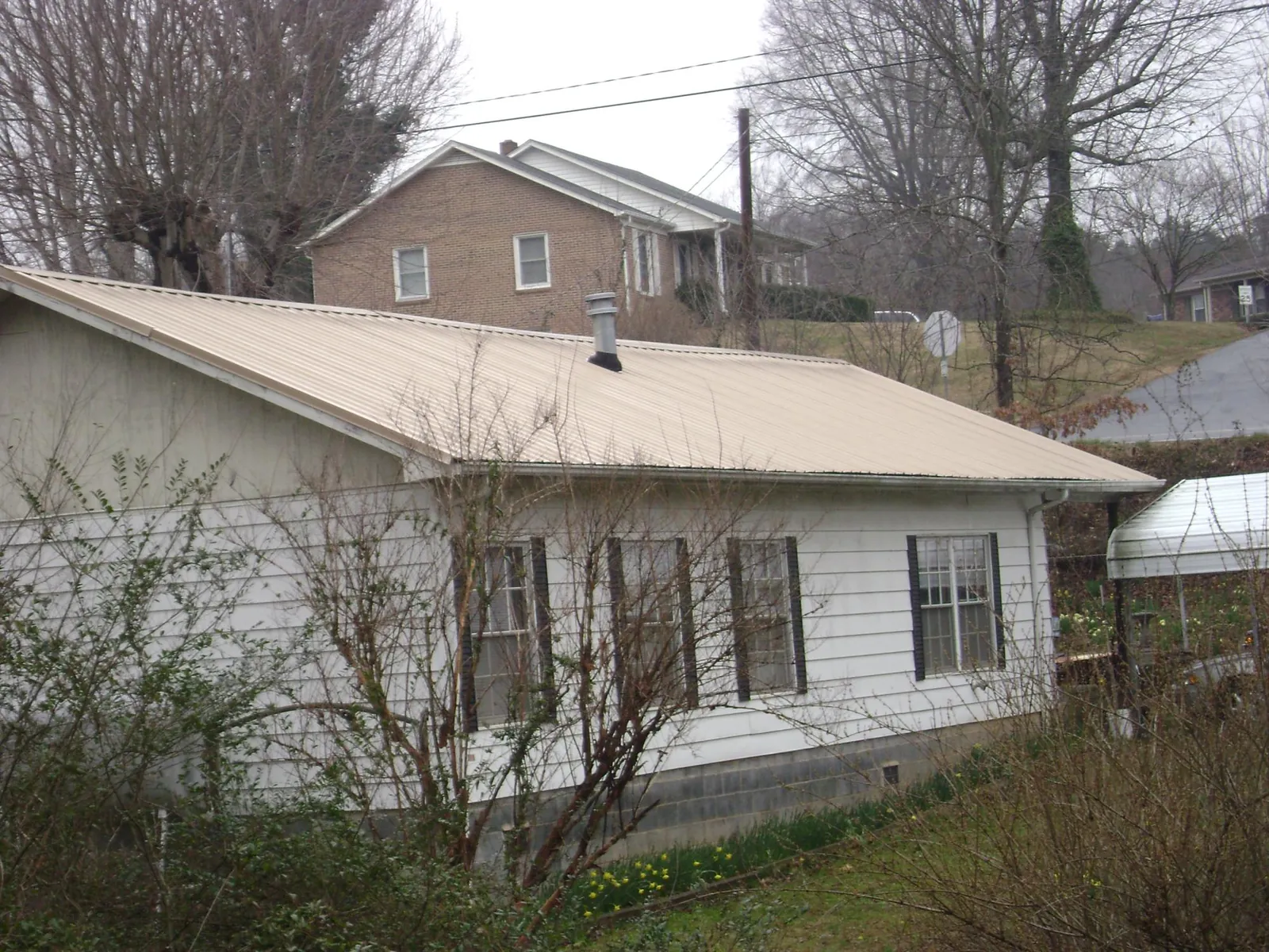 Tan metal roof on a white sided house set into a hillside — Commercial Roofing by Roofing Brothers in Kasson
