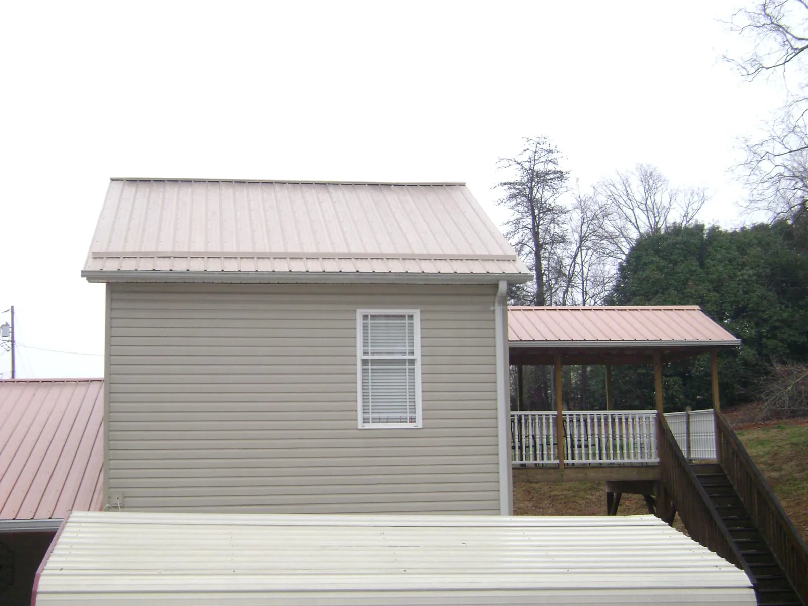 Tan metal roofs on a two story addition and attached porch, from a Roof Replacement job in Kasson